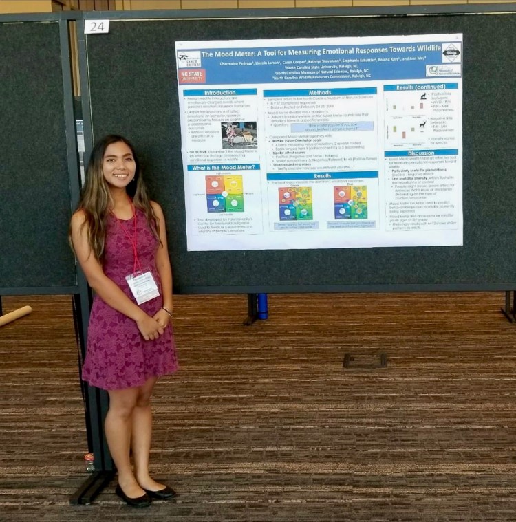 A young, professionally-dressed woman standing next to a research poster. 